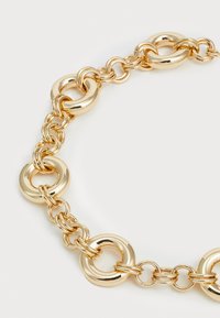 Pulseira de corrente de ouro com elos circulares entrelaçados. Acabamento metálico suave e brilhante, com tamanhos de elo variados para aumentar a textura.