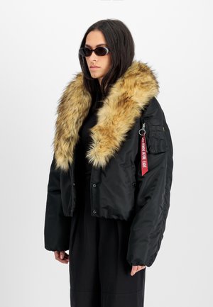 Mustat lyhythihaiset bomber-takit, joissa on suuri tekoturkiskaulus, vetoketjullinen tasku ja punainen label. Litteä rakenne ja pehmustettu muotoilu.
