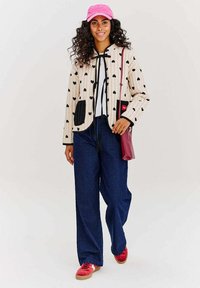 Lemované sako s čiernymi srdcovými vzormi na béžovom pozadí, v kombinácii s voľnými modrými džínsami a červenými teniskami. Súčasťou sú aj ružová čiapka a malá taška.