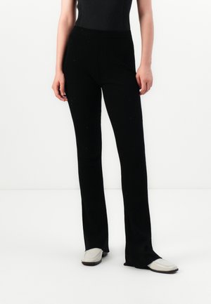 Zwarte geribbelde gebreide broek met een strakke fit, uitlopende zoom en elastische tailleband. Draagt met lichtgekleurde instappers.