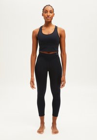 Zwarte atletische cropped tanktop en strakke leggings, gemaakt van een gladde stof. Beschikt over een slank ontwerp met een hoge tailleband en minimale naden.