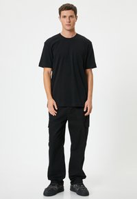 Sort kortærmet t-shirt med brystlomme, parret med løstsiddende sorte cargo-bukser med sidelommer. Tekstureret stof.