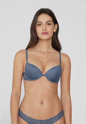 Sostén de encaje en azul pizarra con un escote pronunciado, tirantes ajustables y textura floral. Combinado con un bikini de encaje a juego que presenta un borde festoneado.