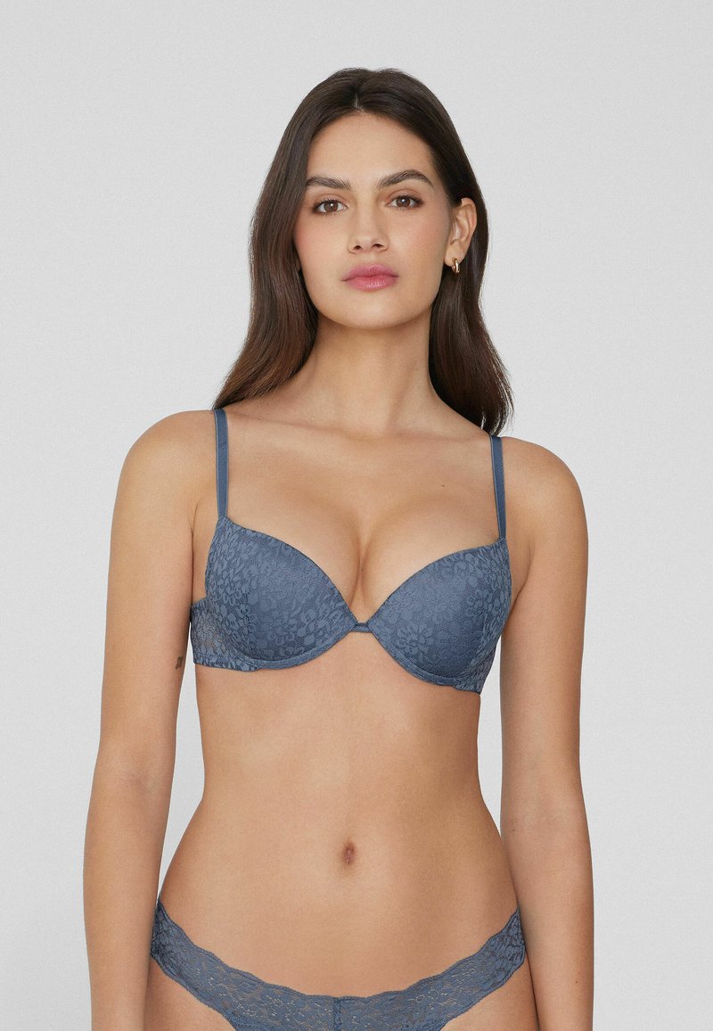 Spitzen-BH mit tiefem Ausschnitt in Schieferblau, verstellbaren Trägern und floraler Textur. Kombiniert mit passendem Spitzen-Bikiniunterteil mit gewelltem Saum.