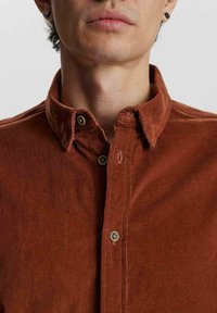 Rostfarbene Cordhemd mit Button-Down-Kragen, aus strukturiertem Stoff mit sichtbaren Nähten.