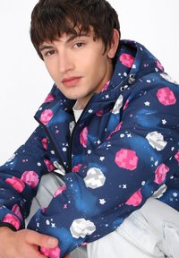 Giacca blu navy con motivi di pianeti rosa e bianchi, dotata di chiusura con zip e cappuccio regolabile. Realizzata in tessuto leggero e testurizzato.