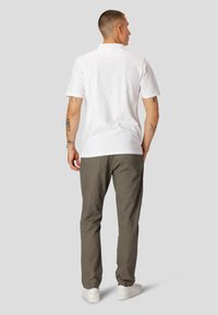 Hvid polo t-shirt med korte ærmer, tekstureret stof og krave. Parret med olivengrønne bukser og hvide sneakers. Simpelt design, ingen synlige logoer.