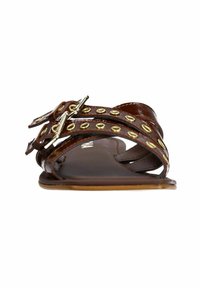 Bruine gepatineerde leren sandaal met twee gespsluitingen, gouden ronde studs, platte zool en open teenontwerp. Glad textuur en minimalistische stijl.