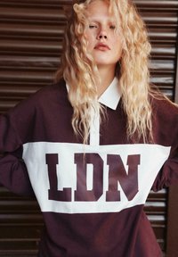 Bordeaux- og hvid langærmet polo-shirt med et stort "LDN" print på brystet, klassisk krave og blød tekstur.
