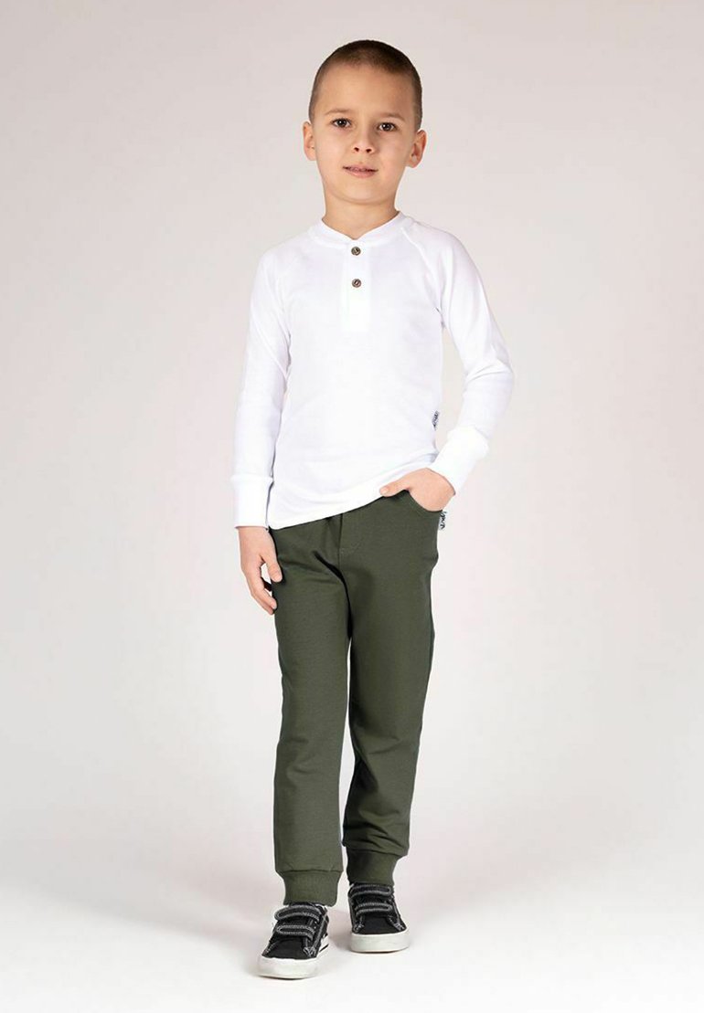 Biała koszulka henley z długim rękawem i trzema guzikami, zestawiona z oliwkowo-zielonymi spodenkami dresowymi i czarnymi trampkami z białymi podeszwami.