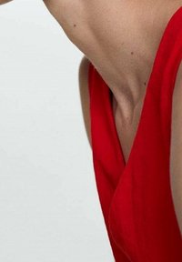 Indumento senza maniche rosso con scollo a V profondo e texture morbida, mostrato su uno sfondo neutro, che mette in risalto il collo e la caduta del tessuto.