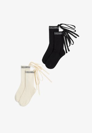 Paire de chaussettes côtelées noires et crème avec bandes logo en haut et longs rubans assortis attachés pour nouer autour du mollet.