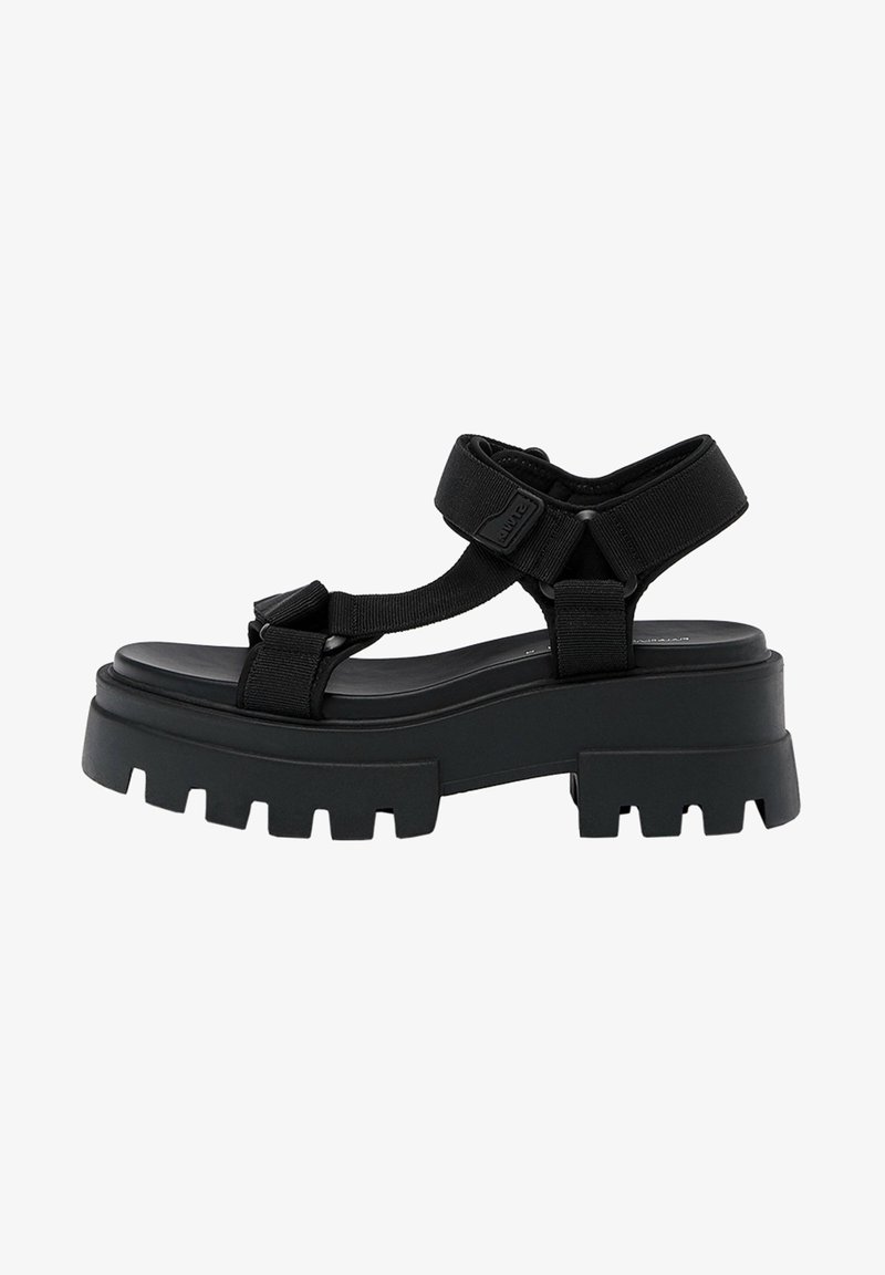 Sandales à plateforme épaisses noires avec des larges brides, des boucles réglables, et une semelle texturée avec de profondes rainures pour une meilleure adhérence.