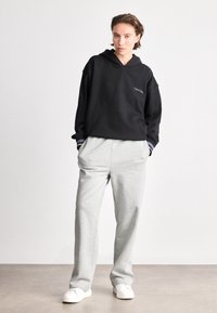 Mustahuoodiline särk, millel on lõdvestatud lõige ja brodeeritud logo. Kombineeritud heledate hallide dressipükstega, millel on elastne vöökoht. Valged tennisetossud.