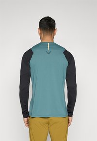 Langarmhemd mit einem türkisfarbenen Körper, schwarzen Ärmeln und einem goldenen Akzent entlang des Rückens. Das Material erscheint glatt mit einer subtilen Textur.