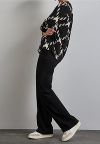 Blusa a righe bianco e nero abbinata a pantaloni neri a gamba larga e sneaker di colore chiaro. Tessuto morbido con vestibilità rilassata e spalle basse.