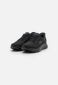 Zapatillas deportivas negras con parte superior de malla, cuello acolchado y suela de goma con detalles texturizados y cierre de cordones.