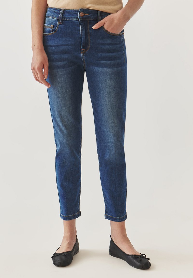 Jeans de mezclilla azul con un corte ajustado, que presentan un diseño de cinco bolsillos, un desvanecimiento sutil y puños enrollados, combinados con bailarinas negras.