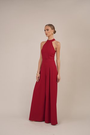 Combinaison sans manches rouge avec un col haut, un design large plissé et un corsage ajusté. Tissu lisse avec des lignes épurées et un minimum de détails.
