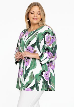 Blumen-Tunika mit weißem Hintergrund, großen grünen Blättern und lila Tulpen. Aus weichem Stoff gefertigt, mit Dreiviertelärmeln und rundem Halsausschnitt.