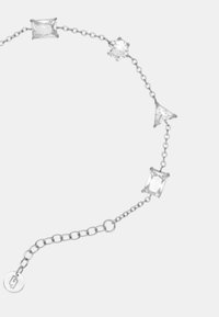 Bracciale in argento con quattro pietre preziose trasparenti: una di forma rettangolare, una triangolare e una rotonda, con un dettaglio a forma di etichetta circolare.