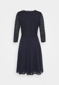 Marineblaues Kleid mit strukturiertem Spitzen-Oberteil und Chiffonrock, langärmlig mit gewelltem Ausschnitt, mit Reißverschluss auf der Rückseite.