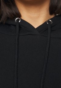 Svart bomulls-hoodie med avslappnad passform, dragsko med metallöglor och ett texturerat stickat mönster vid halslinningen.