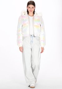 Jachetă scurtă matlasată irizată cu un finisaj lucios, prevăzută cu glugă cu detalii din blană și două buzunare frontale cu fermoar. Asortată cu blugi deschiși la culoare.