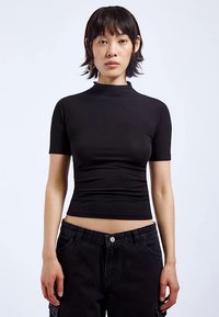 Svart kortärmad topp med hög hals, gjord av stretchigt material. Har en figurnära design och minimala sömmar, kombinerad med högmidjade jeans.