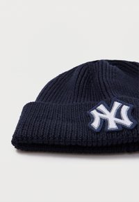 Námornícky pletený čiapka s ohnutým manžetom a bielym výšivkovým logom. Materiál je rebrovaný, čo poskytuje textúru a teplo.