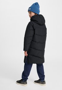 Sort puffjakke med hætte, der har et quiltet design og en lang pasform; parret med marineblå sweatpants og sorte sneakers.