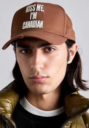 Casquette de baseball marron avec le texte brodé blanc "EMBRASSEZ-MOI, JE SUIS CANADIEN." Tissu doux, forme structurée, accentuée par une visière incurvée.