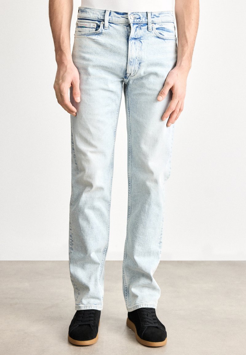 Svijetlo plave traperice opuštenog kroja, izblijedjeli izgled, pet džepova i suptilni detalji poput bora. Nošene s crnim antilop tenisicama.