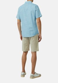 Camicetta azzurro chiaro a maniche corte con una finitura strutturata, abbinata a pantaloni corti beige e sneakers chiare, che mostrano un outfit estivo casual.