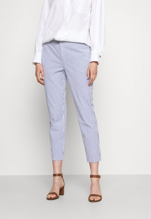 Pantalons rayés bleu et blanc avec une coupe slim, longueur cropped et texture douce, associés à des sandales à talons marron et une chemise blanche.