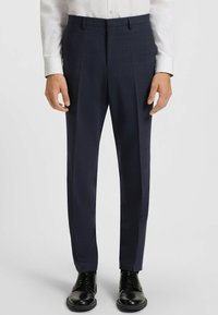 Mörkblå dressbyxor med strukturerat mönster, rak front, sidfickor och skräddarsydd passform, tillsammans med svarta snörskor.