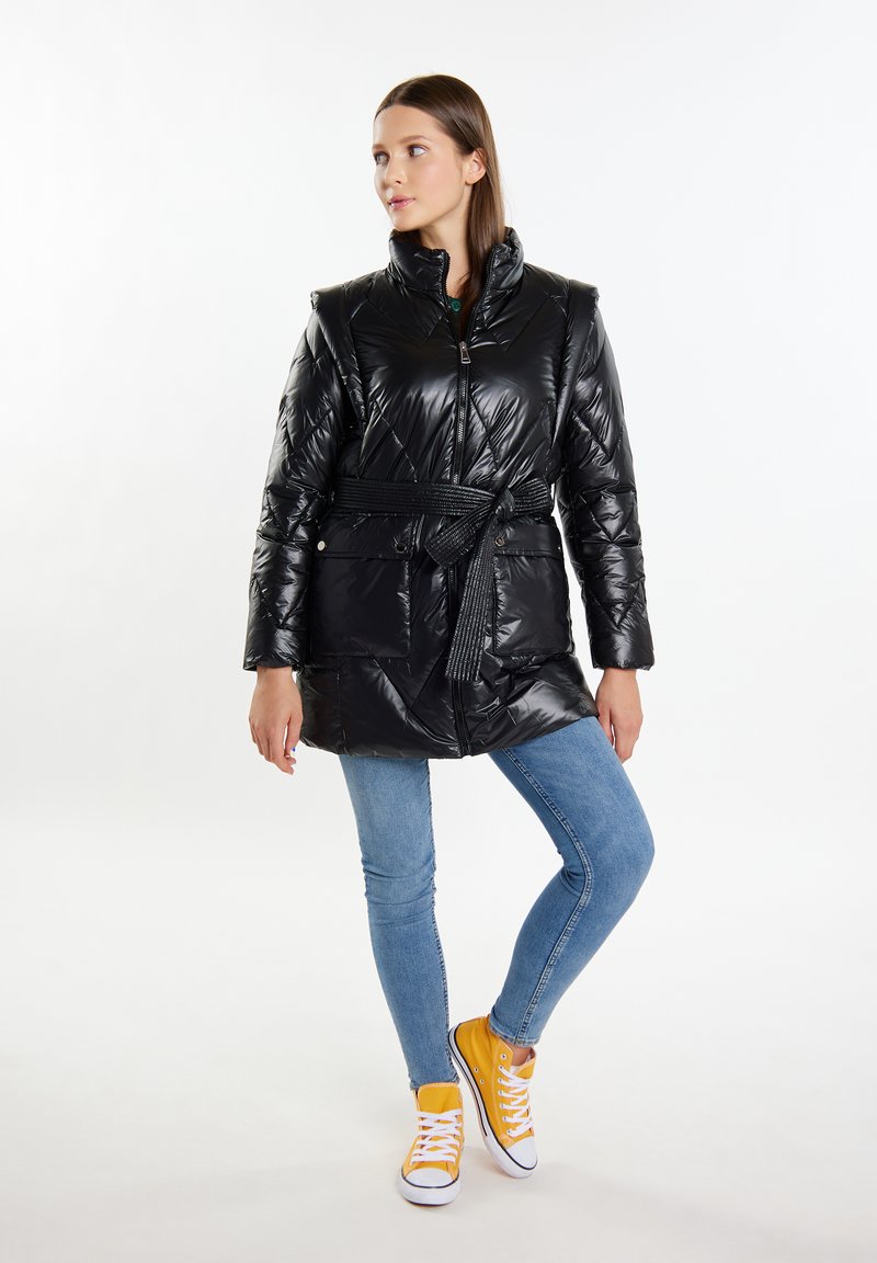Cappotto piumino nero con vita cintata, zip frontale e due tasche anteriori. Abbinato a jeans azzurri e sneakers gialle. Materiale lucido.