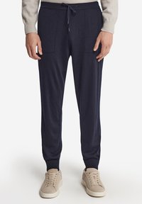 Mörkblå avsmalnande joggers med en mjuk textur, två framfickor, dragsko i midjan och fållade fållar, tillsammans med neutrala sneakers.