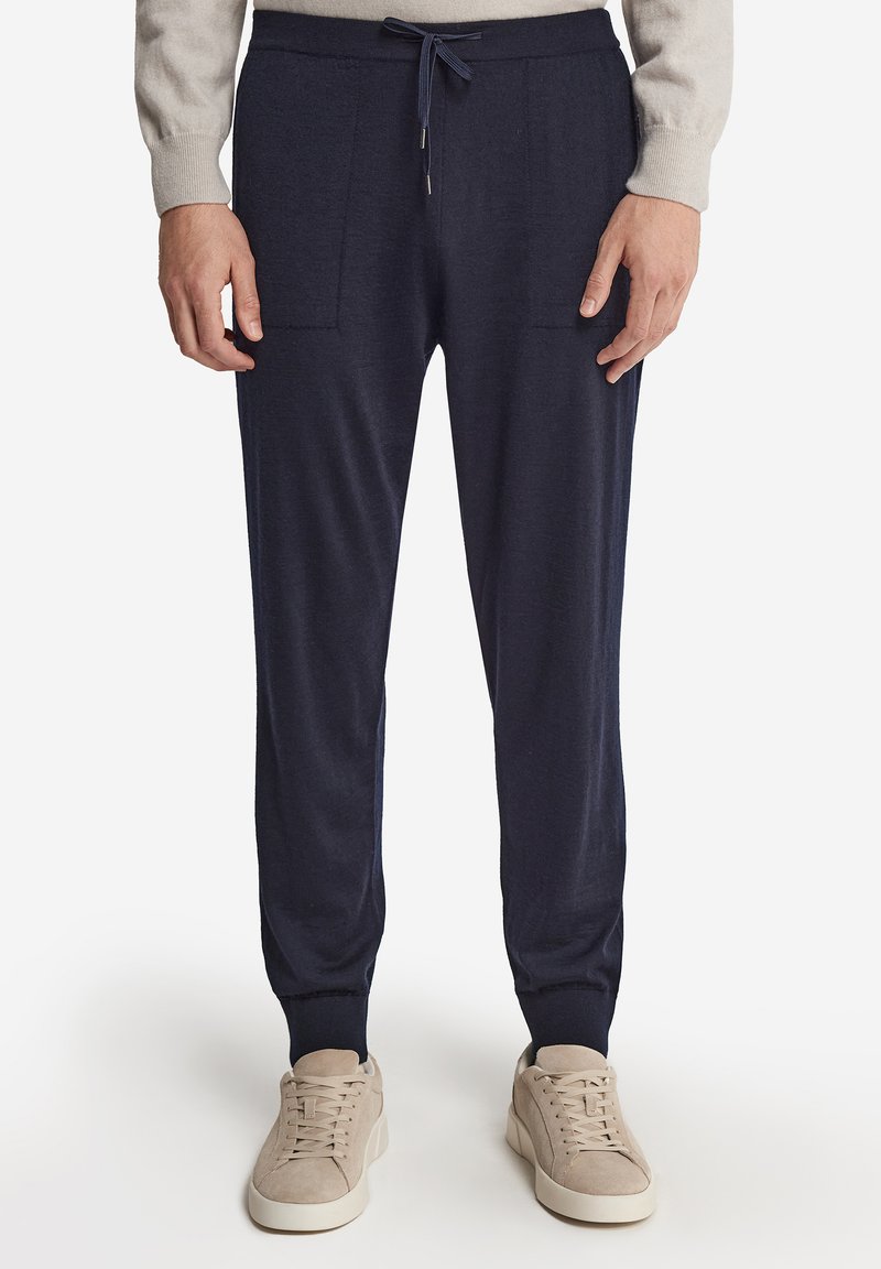 Mörkblå avsmalnande joggers med en mjuk textur, två framfickor, dragsko i midjan och fållade fållar, tillsammans med neutrala sneakers.