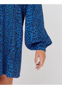 Sininen leopardi-kuvioinen mekko, jossa on pitkät puffihihat ja joustavat hihansuut, valmistettu kevyestä kankaasta, jolla on sileä pinta.