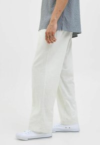 Pantaloni ușori, cu picior larg, dintr-un material texturat alb deschis. Asortați cu adidași albi, evidențiind un stil casual și relaxat.