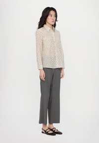 Sheer, light beige shirt with a small, dark leaf pattern, paired with gray wide-leg pants and dark, strappy flats.