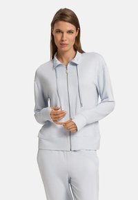 Jasnoniebieski sweter na zamek z wysokim kołnierzem, sznurkiem do regulacji i ściągaczami na rękawach, wykonany z miękkiego materiału, charakteryzujący się luźnym krojem i bocznymi kieszeniami.