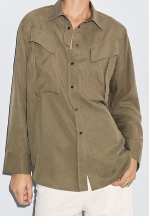 Olive green shirt made of smooth fabric, featuring a front button closure, two chest pockets, and long sleeves with cuff details.