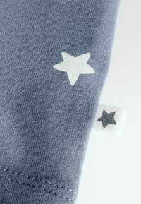 Le tissu en coton bleu présente un grand motif d'étoiles blanches et une petite étiquette grise en forme d'étoile. Texture lisse avec des coutures soignées le long de l'ourlet.