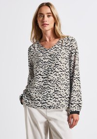 Top a maniche lunghe con scollo a V in tessuto leggero, caratterizzato da uno sfondo beige con motivi astratti neri e polsini a costine.
