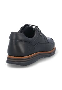 Zapato de cuero negro con textura lisa, que presenta un diseño de cordones, un cuello acolchado y una suela marrón contrastante. Incluye un sutil detalle de marca.