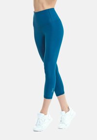 Cyan hoge taille leggings met een gladde textuur, knielange snit en verstevigde naden. Gepaard met witte sportschoenen.