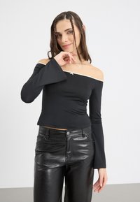 Schwarzes Off-Shoulder-Top mit langen, ausgestellten Ärmeln und weißen Akzenten. Weiches, dehnbares Material mit einem kleinen dekorativen Sternakzent am Ausschnitt.