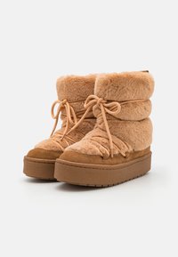 Bottes de cheville marron, doublées de fourrure, avec une texture pelucheuse, une forme arrondie, un système de laçage ajustable et une semelle en caoutchouc épaisse et texturée.